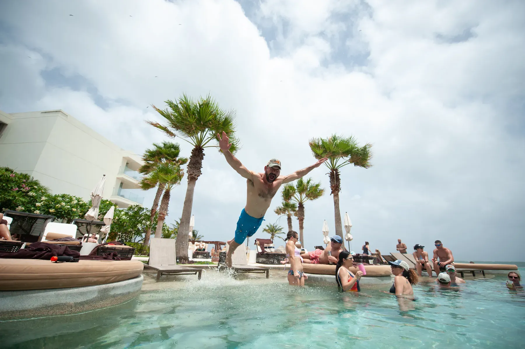 A guest leaps into the resort pool with arms spread as others cheer from the water
