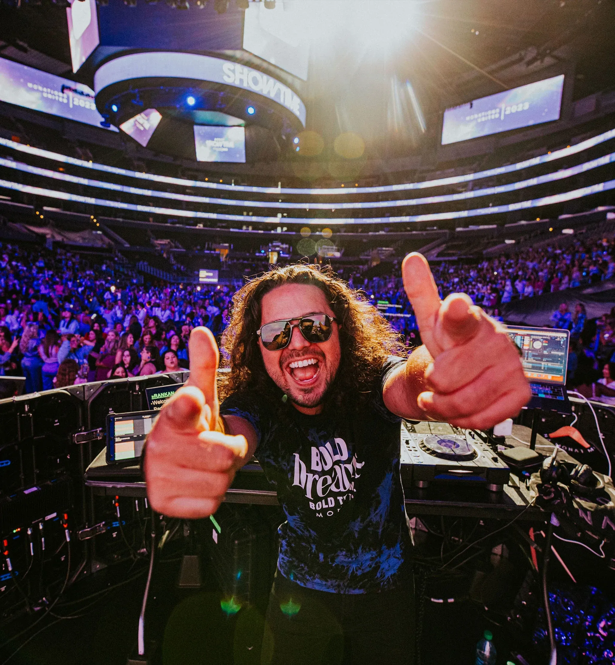 Grinning DJ points at the camera from his booth with a packed Monat Showtime arena behind him