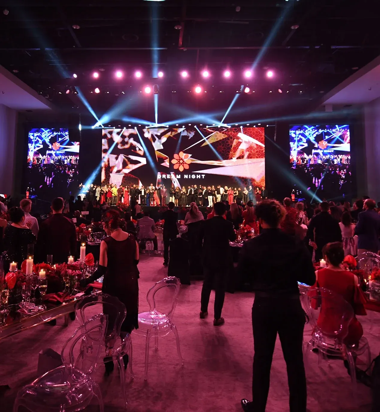 Gala guests at candlelit red-rose tables face a stage filled with people under Dream Night screens