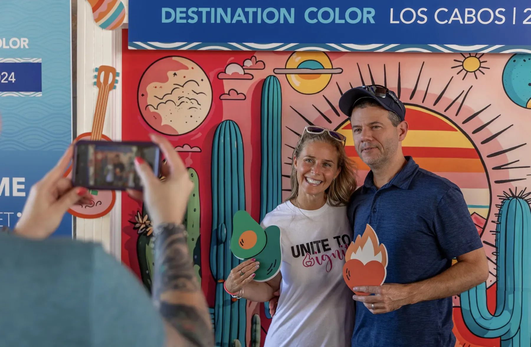 Two guests pose with props in front of the illustrated Destination Color Los Cabos photo wall