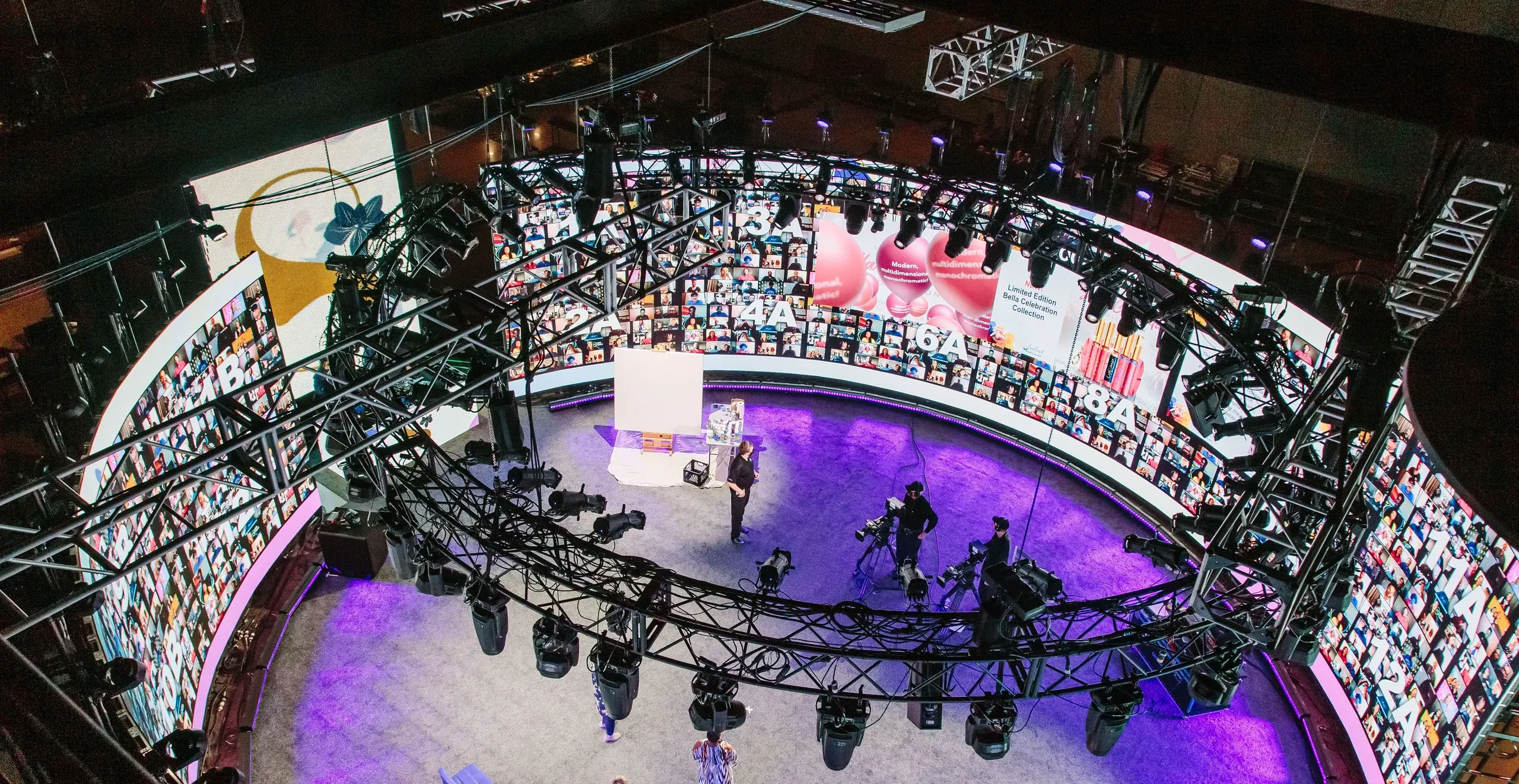 Overhead view of a round broadcast set encircled by numbered virtual-attendee LED walls, lighting truss and cameras