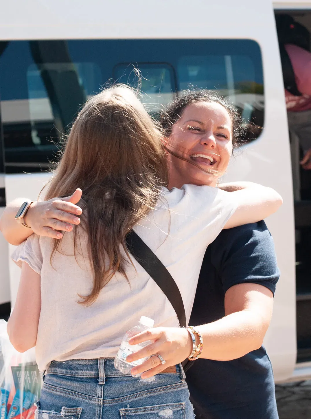 Two IDLife guests hug at arrival beside the airport shuttle