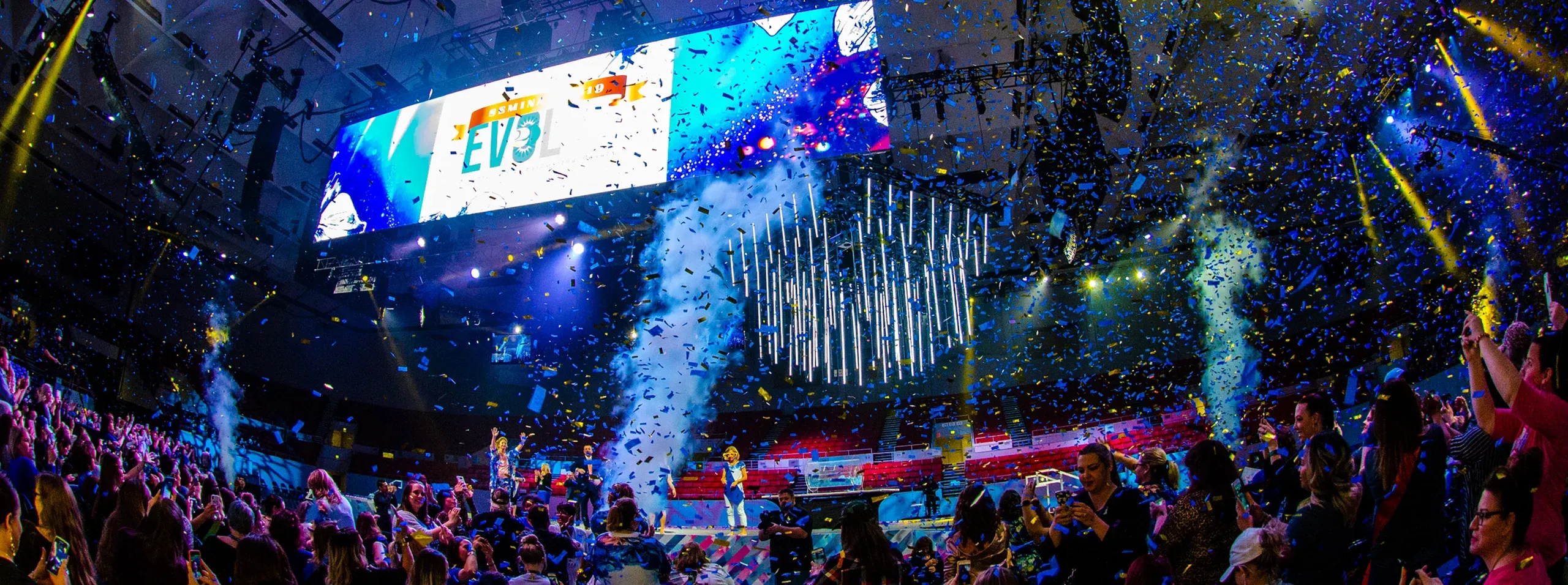 Confetti and CO2 jets burst over a cheering arena crowd beneath an EVOL video screen and hanging LED tubes