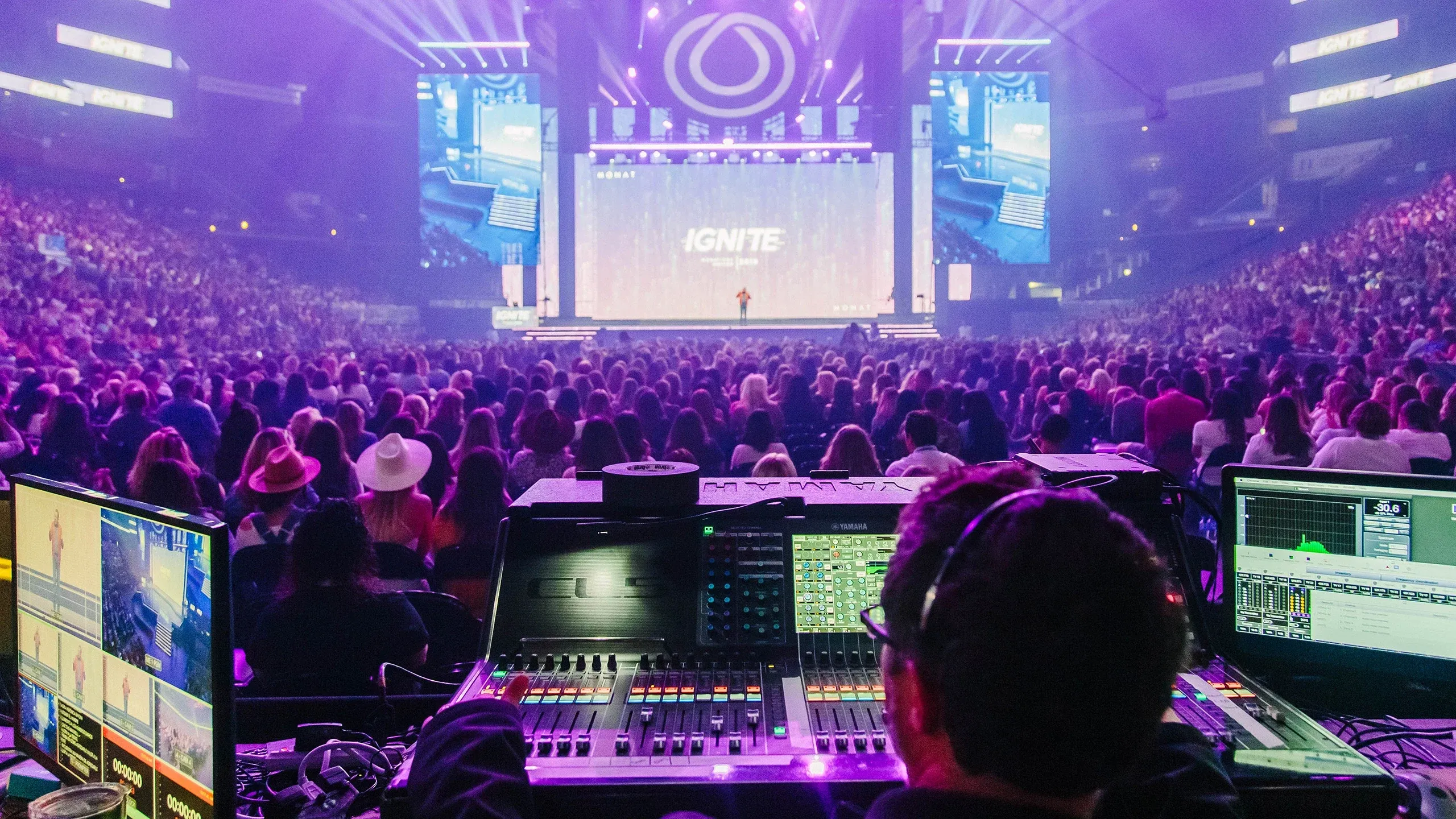 Audio engineer at a Yamaha mixing console facing a packed arena and an IGNITE-branded stage under purple light