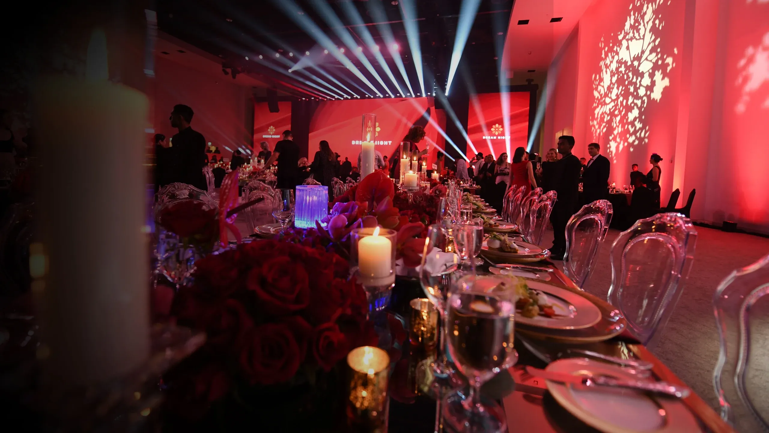 Candlelit banquet table with red roses and crystal glassware as guests mingle under Dream Night screens