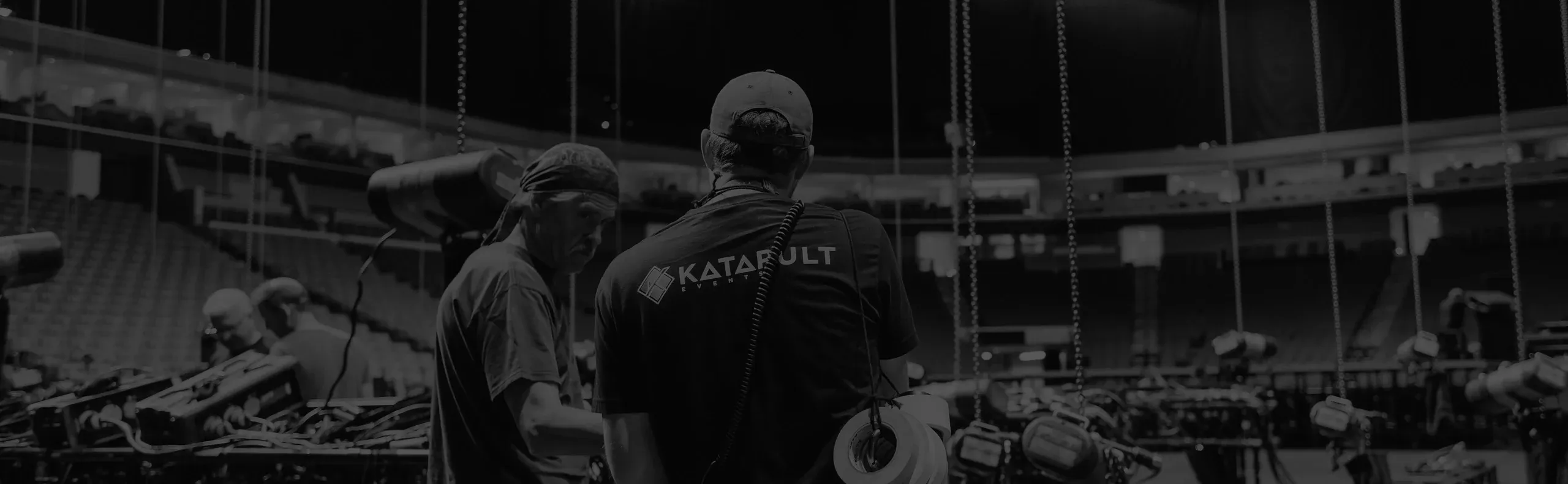 Black-and-white shot of crew in Katapult Events shirts during load-in, chain motors hanging in an empty arena