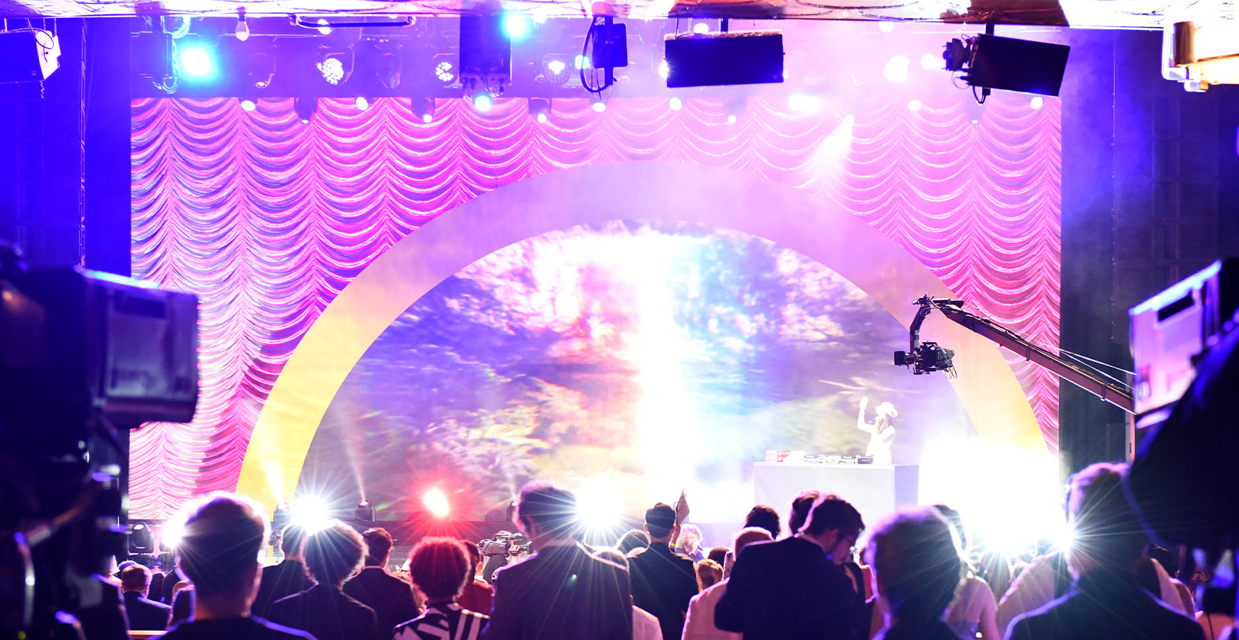 dj wearing black leather jacket with arms raised to crowd in a spotlight